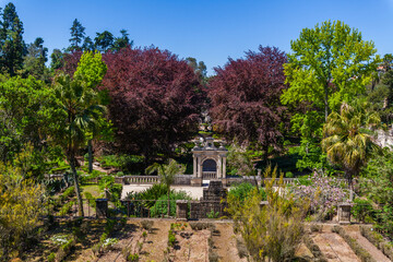 A picturesque garden with a stone archway, surrounded by lush greenery and diverse plant life