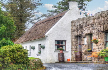 A whitewashed, thatched roof cottage, with two rain barrels and a stone garage, is ready to welcome...