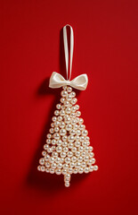 A stylish and elegant white pearl Christmas tree decoration in the shape of an ornament with a bow, set against a red background, decorated with pearls.Minimal creative holiday concept.copy space,flat