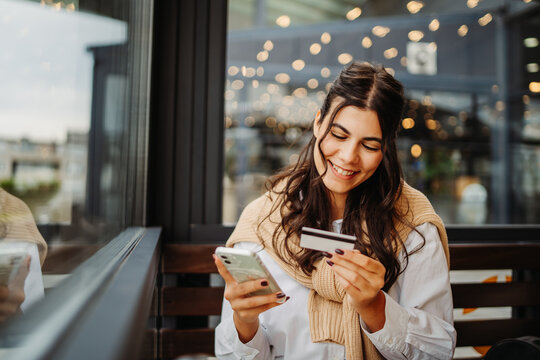Young caucasian woman using credit card in cafe to pay from her phone	
