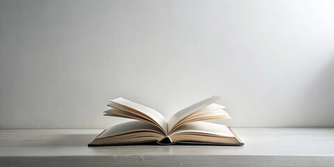 Fototapeta premium Open book resting on a pristine white surface against a bright white wall