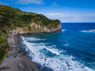 Aerial drone view of Azores islands coast with black sand beach. Praia dos Moinhos landscape in Sao Miguel, Portugal. Atlantic ocean shore with cliffs