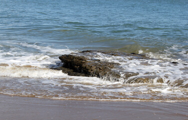 Waves crashing against a rocky outcrop partially submerged in the ocean at a beach