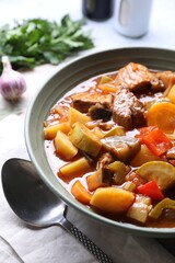 Delicious stew with vegetables in bowl and spoon on table, closeup