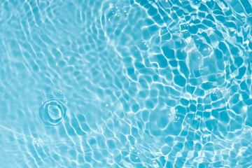 Blue water with ripples on the surface. Defocus blurred transparent blue colored clear calm water surface texture with splashes and bubbles. Water waves with shining pattern texture background.
