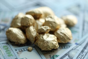 Small pile of golden nuggets and big amount of hundred US dollar bills