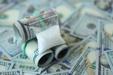 Small cocaine dose in plastic ziplock packet lies on big amount of american currency banknotes
