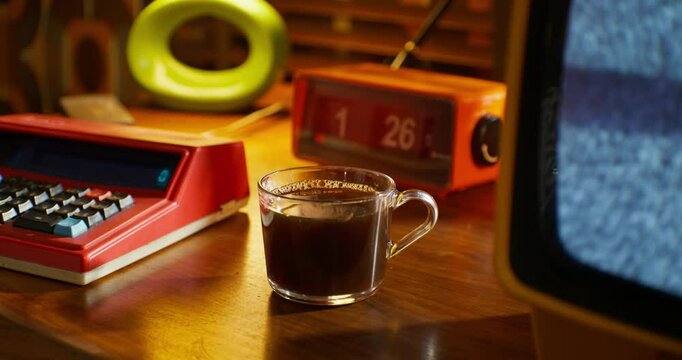A cup of coffee stands near the monitor with ripples on the screen. A desktop in a retro office