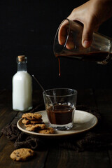 Hot chocolate drink or liquid poured into a glass served with chocolate cookies put on a wooden table