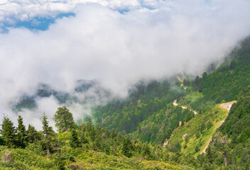 Bright clouds hover above a lush mountain landscape under clear blue skies