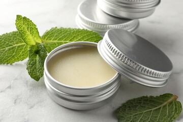 Mint lip balms and green leaves on white marble table, closeup. Cosmetic product