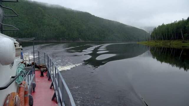 Zeya Reservoir. A boat sails along the calm waters of the lake among green coniferous hills.