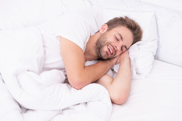 Man sleeping at night. Sleepy man lying on bed sleeping at white bedroom. Asleep young man sleeping. Resting peacefully in comfortable bed. Lying with closed eyes. Deep male sleep. Refreshing nap