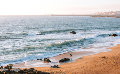 Beautiful sunset at praia de lavadores beach in vila nova de gaia, portugal, with a man picking up...
