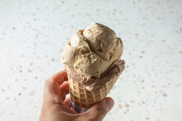 A view of a hand holding a two-scoop ice cream cone.