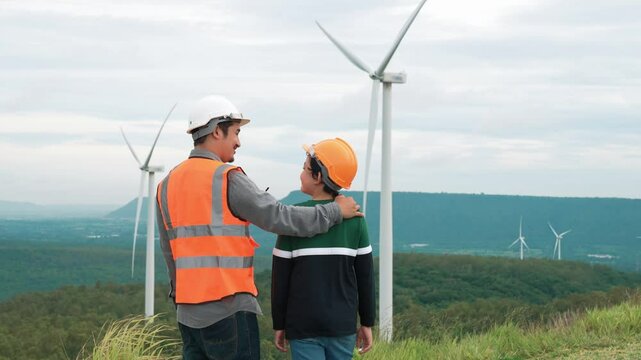 Engineer with his son on a wind farm atop a hill or mountain in the rural. Progressive ideal for the future production of renewable, sustainable energy. Energy generation from wind turbine.