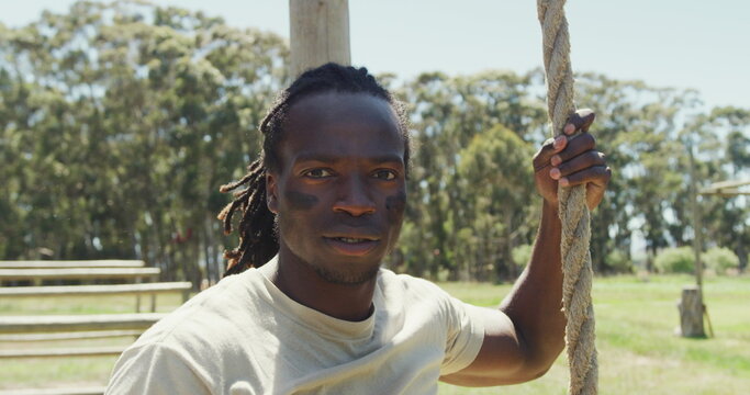 Fit african american male soldier with deadlocks climbing down rope on army obstacle course - Powered by Adobe
