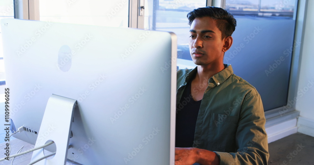 Poster executive using mobile phone while working on computer at desk