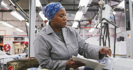 Fototapeta premium African American female car mechanic working in a township workshop, painting a body of a car in slo