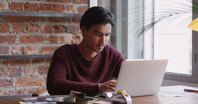 Front view of biracial man with short dark hair, working at home, sitting at the table in his sittin