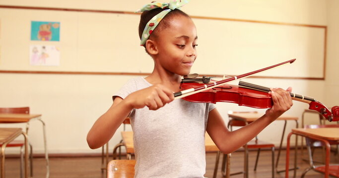 Cute pupil playing violin in classroom at the elementary school