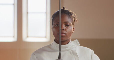 Portrait of a confident focused biracial female fencer athlete during a fencing training in a gym, s
