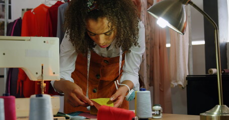 Front view of African American female fashion designer looking at cloth samples in workshop