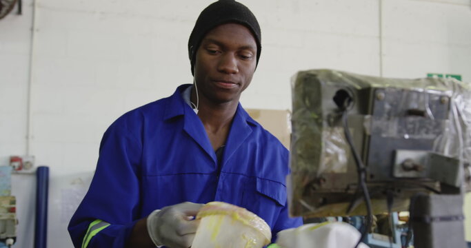 Front view close up of an African American man wearing gloves, overalls and a hat working at a facto - Powered by Adobe