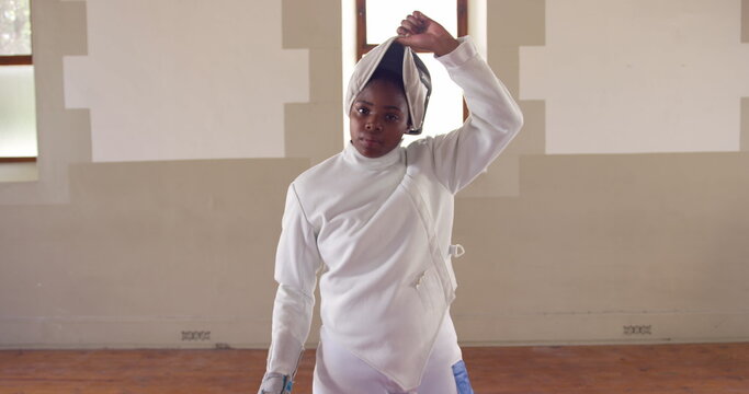 Portrait of a happy biracial female fencer athlete during a fencing training in a gym, walking weari