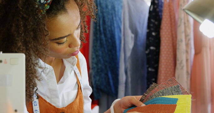 Front view of African American female fashion designer looking at cloth samples in workshop