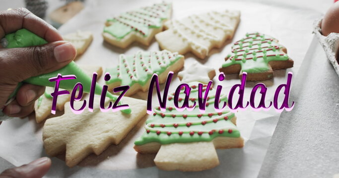 Feliz navidad text in purple over african american hand decorating christmas cookies - Powered by Adobe