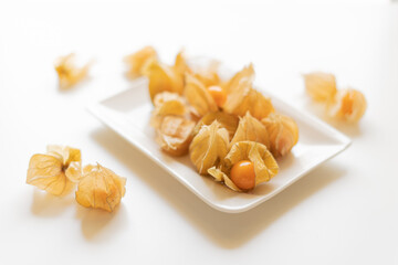 Macro photo of ripe orange physalis on white plate against white background