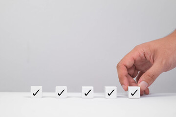 A hand places a block with a checkmark in a row of similar blocks, symbolizing success or task...