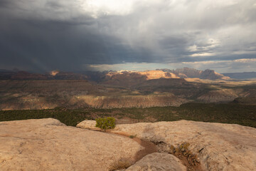 A mixture of sunlight and cloud shadows lays over the rugged landscape of Southern Utah, USA from a viewpoint on the edge of Smith Mesa looking towards Zion NP while a summer storm rolls past.