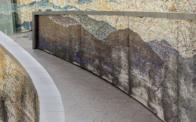 A sloping walkway leading down to a park in a high-rise building with cladding in the shape of an arch are decorated with colorful Stained glass scraps mosaic.