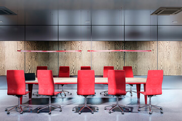 Modern boardroom interior with red chairs and wooden accents, featuring a long table and sleek...