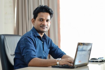 Portrait of handsome young indian man using laptop and earphone at home office