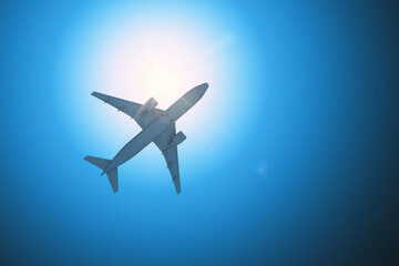 Airplane flying against bright sunlight in clear blue sky viewed from below. 3D Rendering