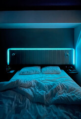 Aesthetic photo of the bedroom's night interior. a bed with two pillows and an open blanket and a turquoise neon night light above the bed.
