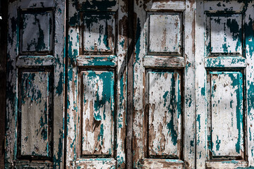 Shut.  Four old window shutters with peeling white and green/blue paint in partial shadow and sunlight.