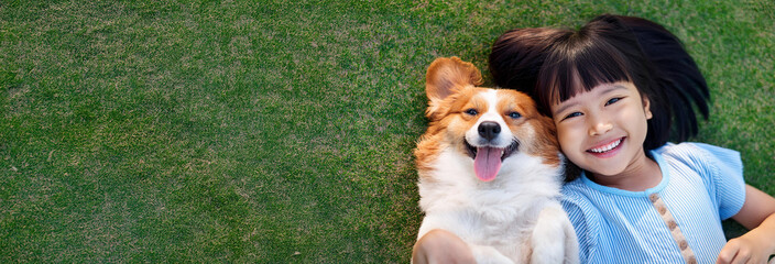 犬と一緒に芝生に寝転んでいるアジア人の幼い少女。（A young Asian girl is lying on the grass with her dog.）
