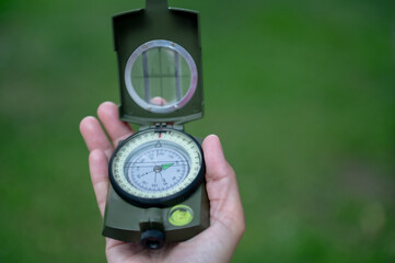 A hand holds a compass open against a blurred green background, symbolizing navigation and outdoor exploration.