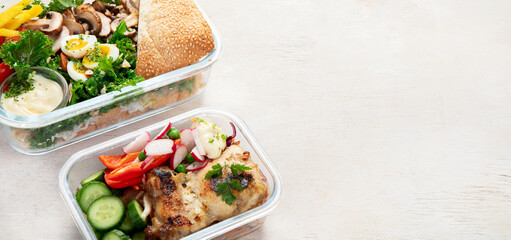 Lunch box containers with grilled chicken breast and fresh vegetable salad.