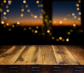  Festive background. The backdrop. An empty wooden table by the window. Festive garlands on the window. Evening. Sunset. Defocus lights. Bokeh. Copy space