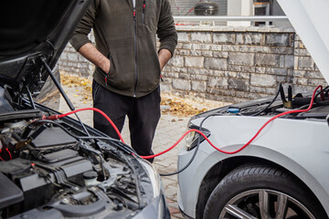 Man jump-starting a car using jumper cables outdoors