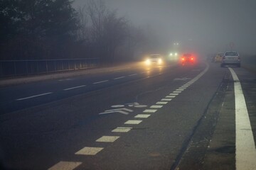 Car traveling on the foggy road with headlights or headlamps on. Low visibility - Dangerous driving of cars in winter in bad weather.