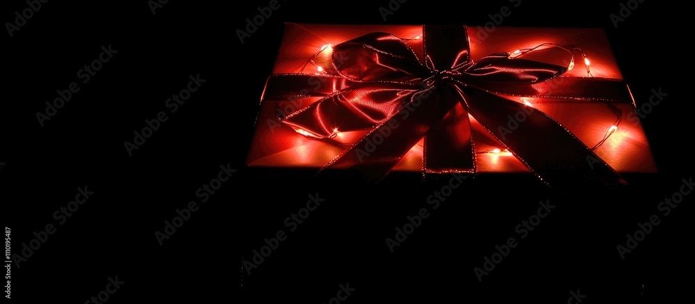 Poster elegant gift box with glossy red ribbon and twinkling lights creating a festive atmosphere on a dark