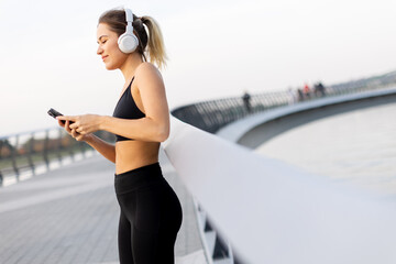 A young woman enjoys a peaceful moment listening to music on a tranquil bridge during sunset by the water