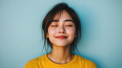 Joyful young woman in yellow shirt smiling with closed eyes against a vibrant blue background capturing happiness and positivity