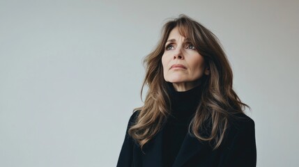 Fototapeta premium Middle aged woman in black outfit displaying a painful expression against a minimalist white background conveying emotional distress and vulnerability